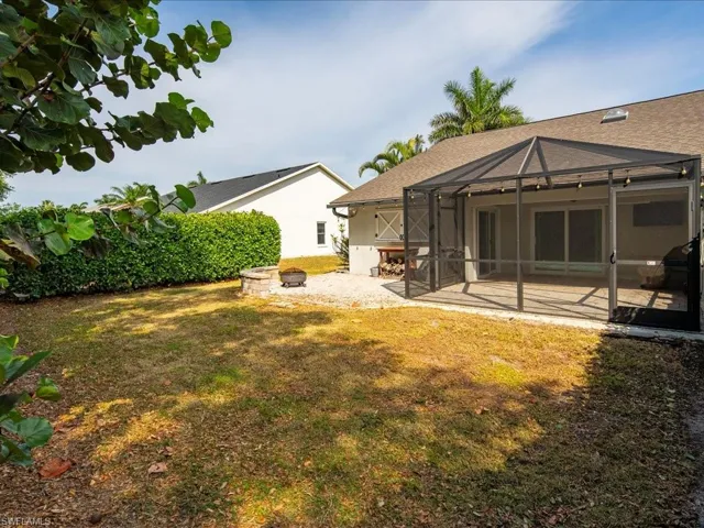 Rear view of house featuring glass enclosure, an outdoor fire pit, stucco siding, a patio, and a lawn