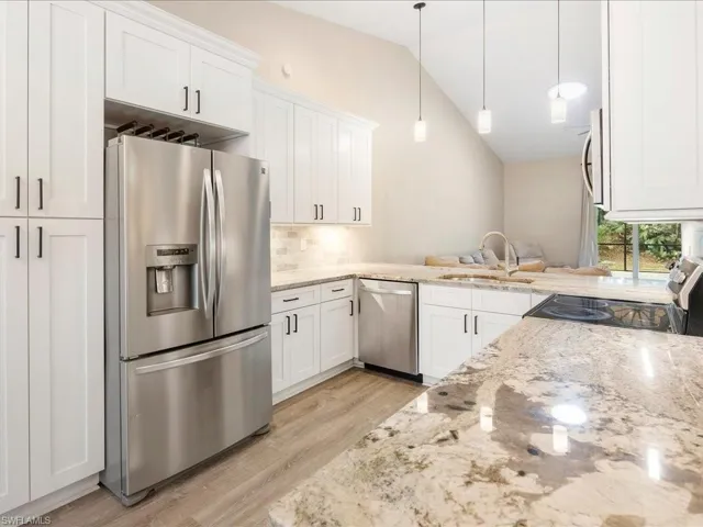 Kitchen with white cabinetry, lofted ceiling, a sink, light stone counters, and appliances with stainless steel finishes