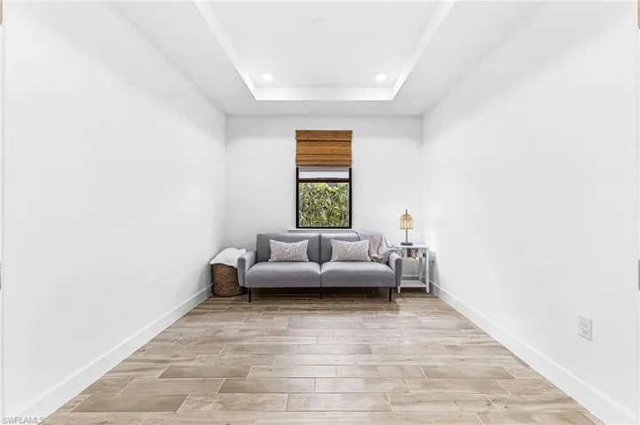 Room featuring wood-finish flooring, white baseboards, a single window with a wood-tone blind, and a recessed ceiling tray with integrated lighting