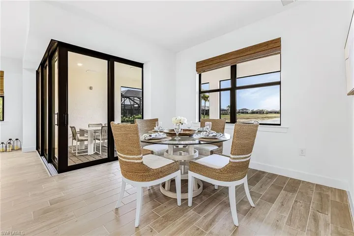 Dining area featuring light wood-finish flooring, white walls, and a large window with a woven Roman shade