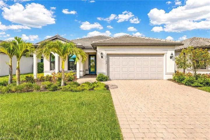 Contemporary residence featuring a paver driveway, an attached two-car garage, a tiled roof, a covered entry with columns, and established landscaping with palm trees