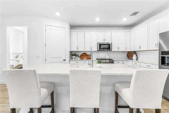 Contemporary kitchen featuring white cabinetry, stainless steel appliances, a white tile backsplash, a large center island with a sink, and recessed lighting