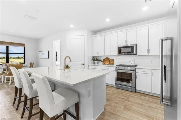 Open-concept kitchen featuring a large island with seating, stainless steel appliances, white shaker cabinetry, light countertops, and wood-finish flooring