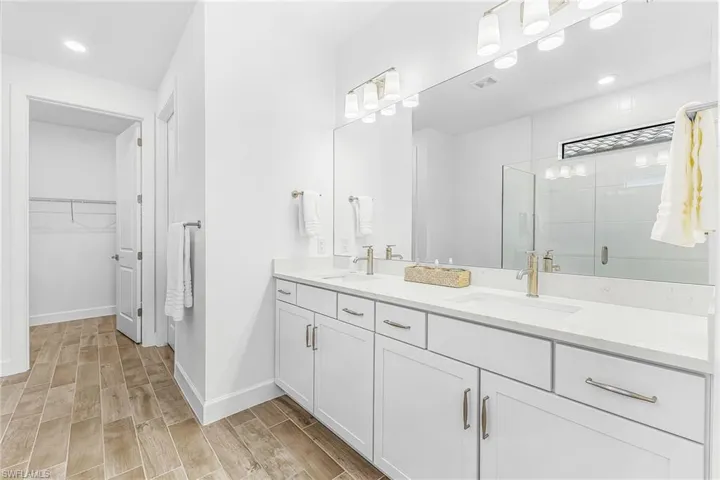 Bathroom featuring wood-finish tile flooring, a dual vanity with white cabinetry, and a spacious glass-enclosed shower