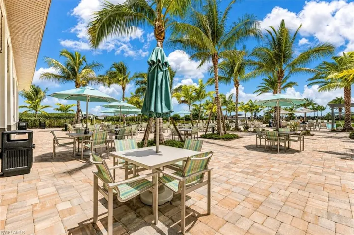 Expansive outdoor patio featuring paver flooring, multiple dining tables with umbrellas, and mature palm trees