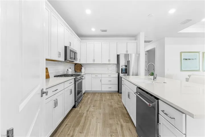 Modern kitchen featuring white shaker cabinetry, stainless steel appliances, a subway tile backsplash, and light wood-finish flooring