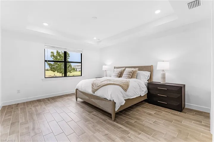 Spacious bedroom featuring wood-finish tile flooring, a large window with black trim, recessed lighting, and a tray ceiling