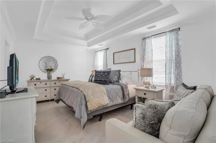 Bedroom with crown molding, ceiling fan, light tile floors, and a raised ceiling