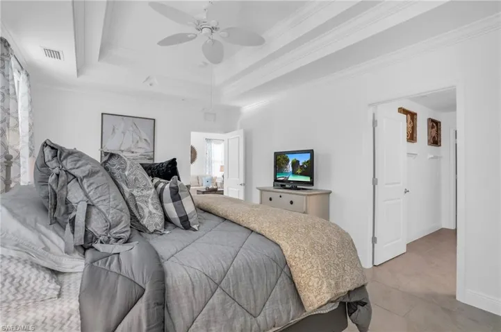 Bedroom featuring a tray ceiling, tile flooring, crown molding, and ceiling fan