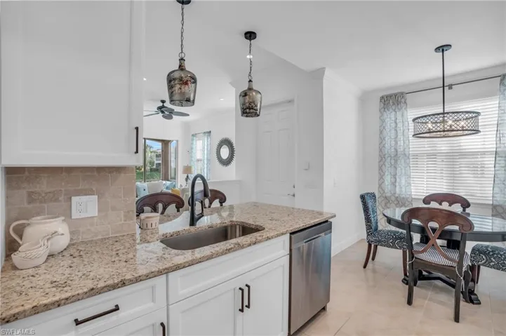 Kitchen featuring tasteful backsplash, white cabinetry, stainless steel dishwasher, sink, and pendant lighting