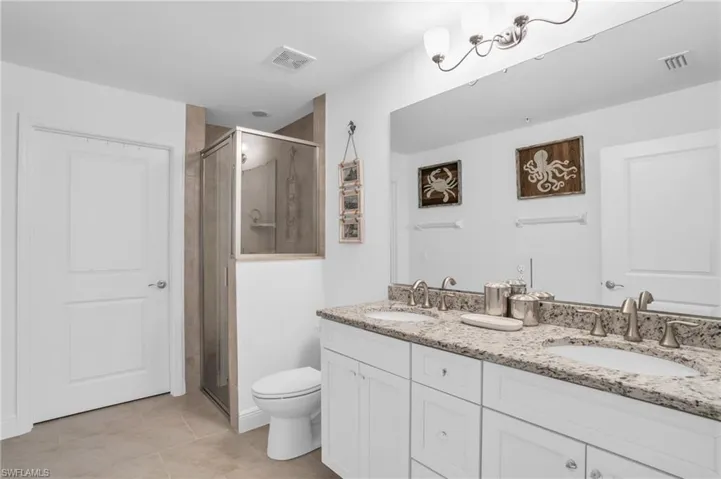 Bathroom featuring a shower with shower door, toilet, tile floors, and dual bowl vanity