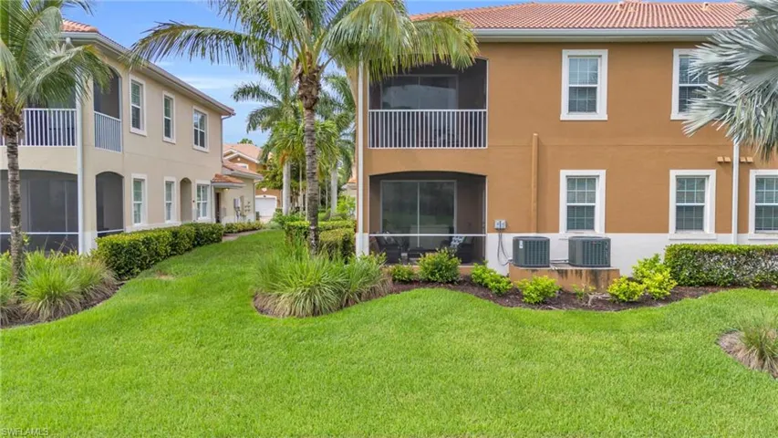 Rear view of house with a balcony, central AC unit, and a lawn
