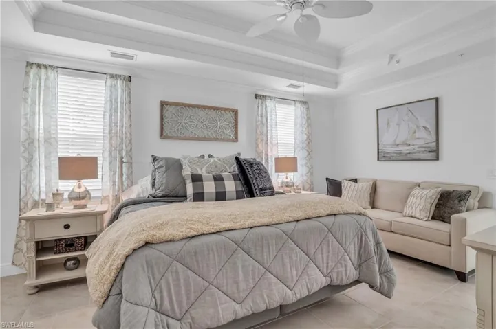 Tiled bedroom with ceiling fan, a raised ceiling, and crown molding