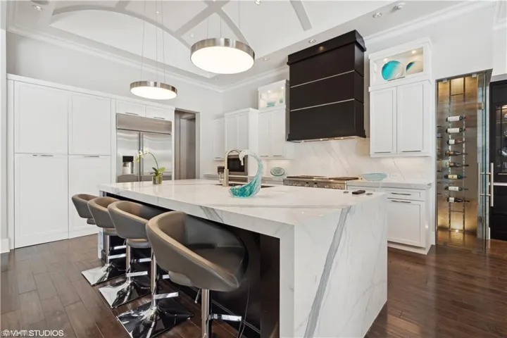 Kitchen with dark hardwood / wood-style flooring, light stone counters, built in fridge, white cabinets, and a kitchen island with sink