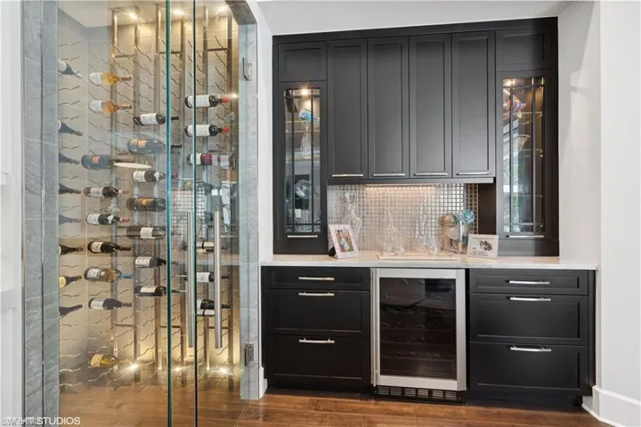 Bar featuring backsplash, dark wood-type flooring, and beverage cooler
