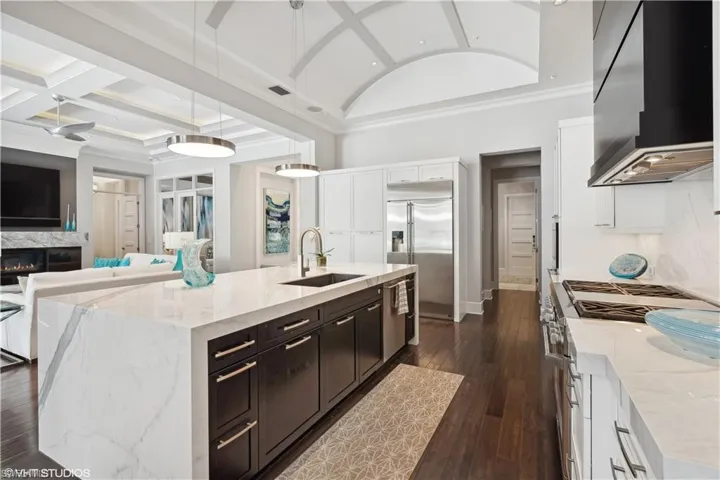 Kitchen featuring an island with sink, sink, white cabinets, and wall chimney exhaust hood