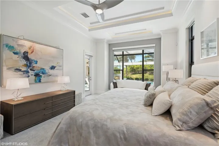 Carpeted bedroom with ceiling fan, access to exterior, a tray ceiling, and crown molding