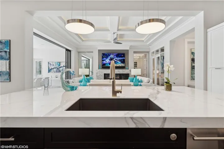 Kitchen featuring decorative light fixtures, sink, coffered ceiling, and light stone counters
