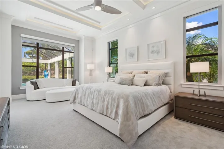 Bedroom with light colored carpet, ornamental molding, ceiling fan, and a raised ceiling