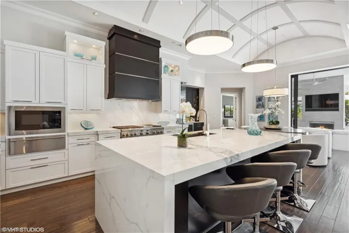 Kitchen with dark hardwood / wood-style floors, a center island with sink, a fireplace, premium range hood, and light stone counters
