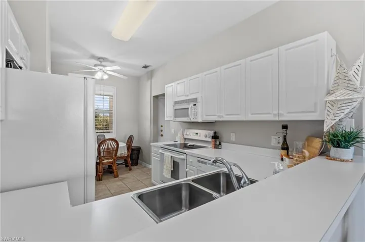 Kitchen with kitchen peninsula, white appliances, sink, light tile patterned floors, and white cabinets