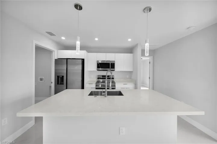 Kitchen featuring appliances with stainless steel finishes, white cabinets, a kitchen island with sink, light stone counters, and decorative light fixtures