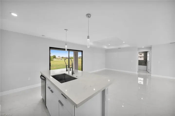 Kitchen featuring an island with sink, sink, hanging light fixtures, and light tile flooring