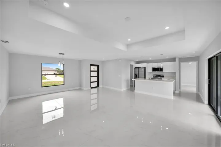Unfurnished living room with sink, light tile flooring, and a raised ceiling