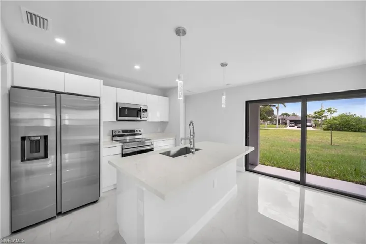 Kitchen featuring stainless steel appliances, pendant lighting, light tile floors, sink, and white cabinets