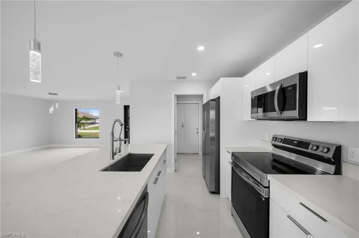Kitchen featuring stainless steel appliances, decorative light fixtures, light tile floors, sink, and white cabinets