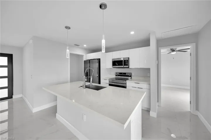 Kitchen with hanging light fixtures, a center island with sink, appliances with stainless steel finishes, white cabinets, and sink