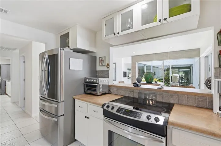 Kitchen featuring white cabinetry, light-toned countertops, tile flooring, and a stainless steel range