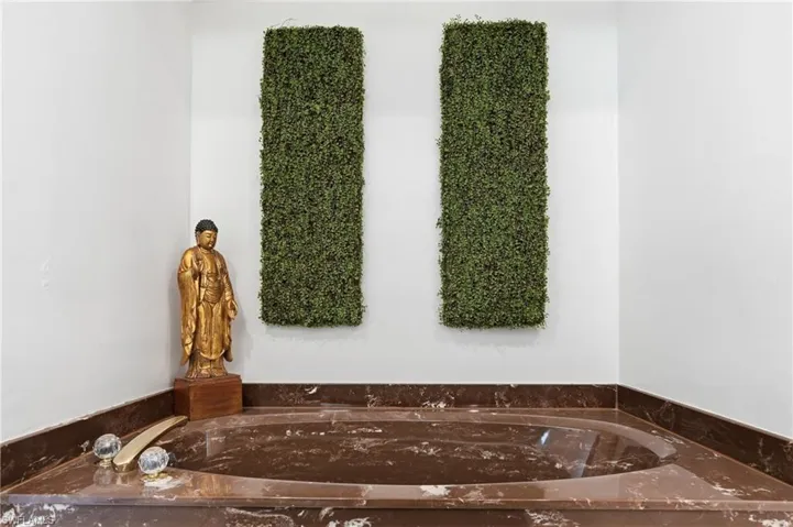 Built-in corner bathtub with a brown veined stone surround and deck-mounted fixtures, complemented by two vertical green wall panels