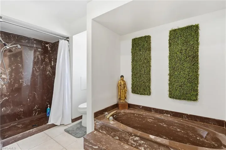 Luxurious bathroom featuring an expansive brown marble-finish soaking tub, a coordinating brown marble-finish shower with a handheld showerhead, and light tile flooring