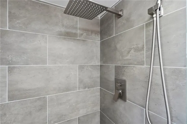 Shower with gray subway tile surround, featuring a square rain shower head, handheld shower fixture, and brushed nickel controls