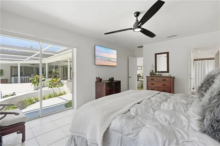 Bright bedroom with sliding glass doors opening to a screened patio, featuring tile flooring, a modern ceiling fan, and white walls
