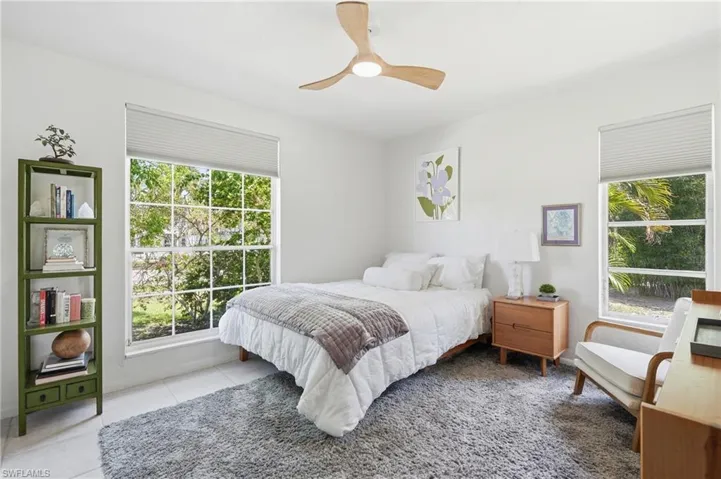 Bright interior space featuring a ceiling fan with integrated lighting, multiple windows with honeycomb blinds, and white tile flooring