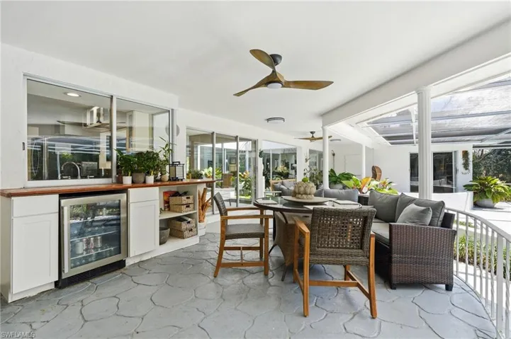 Covered patio with a patterned concrete floor and a full outdoor kitchen featuring a built-in beverage refrigerator, wood-finish countertop, and pass-through window