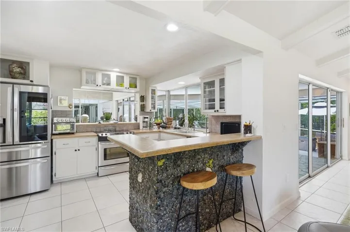 Open kitchen featuring stainless steel appliances, white cabinetry, a stone-clad island with countertop seating, recessed lighting, and tile flooring