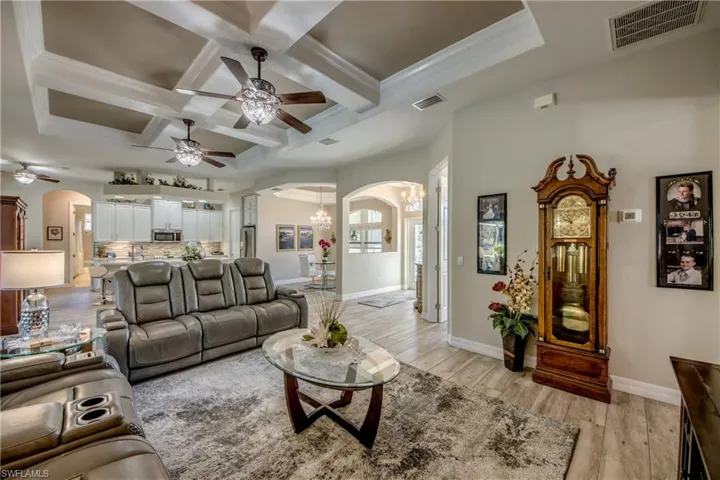 Living room featuring crown molding, ceiling fan with notable chandelier, coffered ceiling, and light wood-type flooring