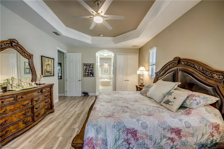 Bedroom featuring ensuite bath, a tray ceiling, ceiling fan, light hardwood / wood-style floors, and a closet