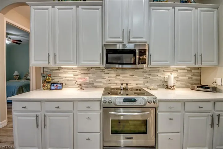 Kitchen featuring decorative backsplash, white cabinetry, and appliances with stainless steel finishes