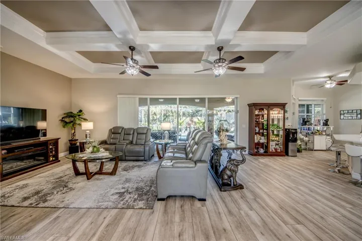 Living room with beamed ceiling, light wood-type flooring, plenty of natural light, and coffered ceiling