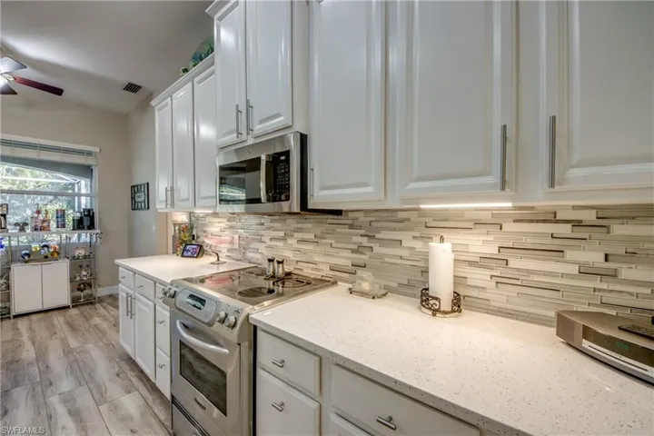 Kitchen featuring light hardwood / wood-style flooring, light stone countertops, appliances with stainless steel finishes, tasteful backsplash, and white cabinetry