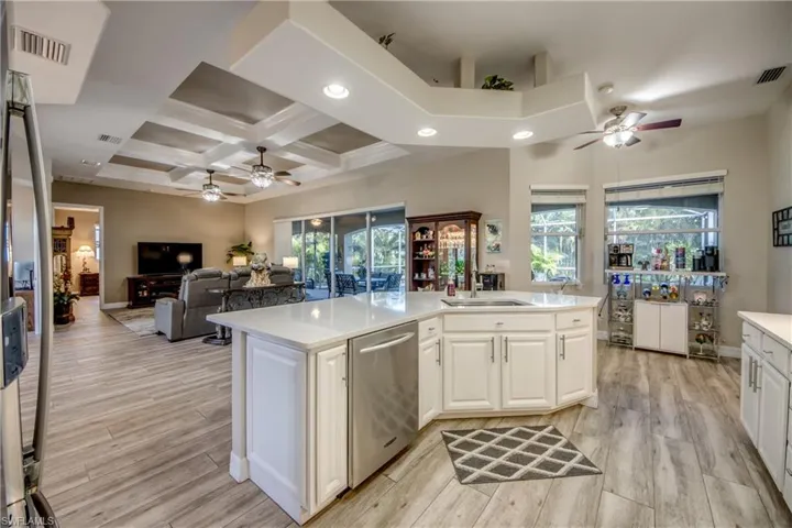 Kitchen with white cabinetry, sink, coffered ceiling, stainless steel dishwasher, and light hardwood / wood-style floors