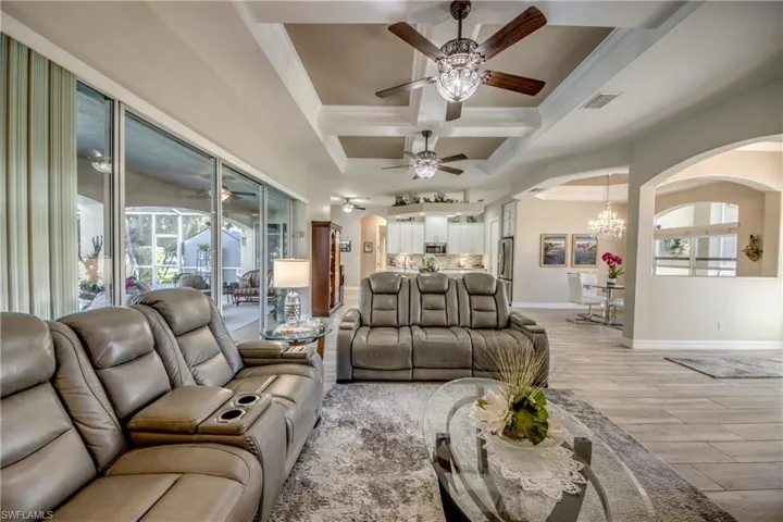 Living room featuring ornamental molding, coffered ceiling, ceiling fan with notable chandelier, beam ceiling, and light hardwood / wood-style flooring