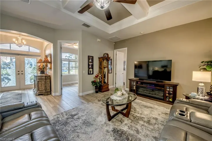 Living room featuring beam ceiling, french doors, coffered ceiling, light hardwood / wood-style floors, and ceiling fan with notable chandelier