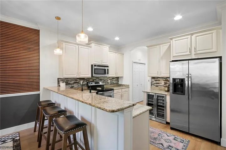 Kitchen featuring appliances with stainless steel finishes, light stone counters, a peninsula, pendant lighting, and arched walkways