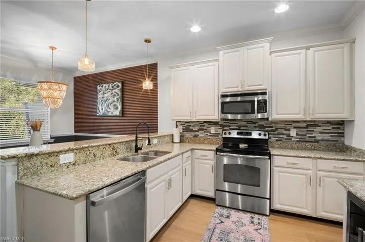 Kitchen with stainless steel appliances, a peninsula, white cabinets, light stone counters, and decorative light fixtures