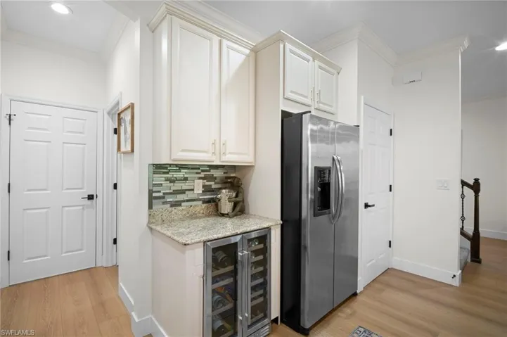 Kitchen with crown molding, light stone countertops, stainless steel fridge with ice dispenser, tasteful backsplash, and wine cooler